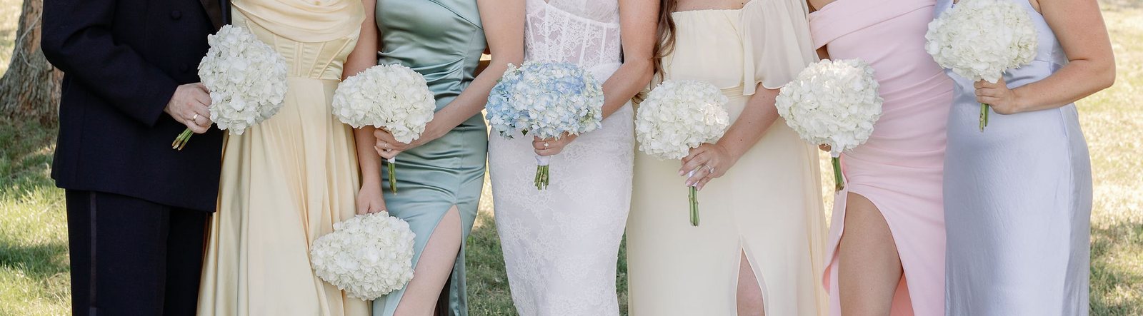 Bridal party in pastel dresses holding white hydrangea bouquets, the bride holding pale blue hydrangeas